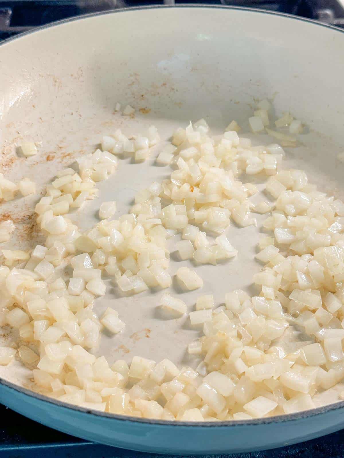 Diced yellow onions being sauteed in a pan.