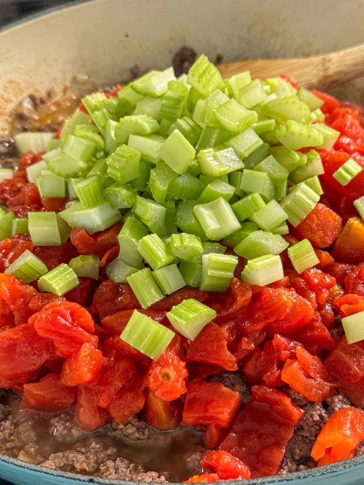 Diced celery, and tomatoes on top of browned ground beef in a pan.