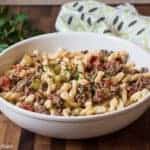 Oma's Spaghetti - Gremelli Pasta with sauce made with ground beef, onions, celery, fresh tomatoes and butter, served in a wide white bowl that is placed on a walnut cutting board, napkin placed nearby, with a little fresh green parsley