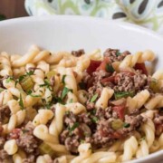 Oma's Spaghetti - Gremelli Pasta with sauce made with ground beef, onions, celery, fresh tomatoes and butter, served in a wide white bowl that is placed on a walnut cutting board, napkin placed nearby, with a little fresh green parsley