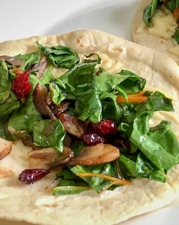 Beautiful Green Leafy Chopped Swiss Chard and Mushroom Wraps on 2 Flour Tortillas served on a white plate.