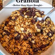 Bowl of homemade honey granola with milk, showing its soft, lightly sweet texture, with a tray of granola blurred in the background.