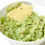 Guacamole with a chip inside a white bowl.