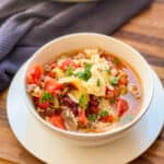Image showing a white bowl of yummy beef and cabbage soup on a walnut cutting board pictured with a blue kitchen towel in upper left corner.