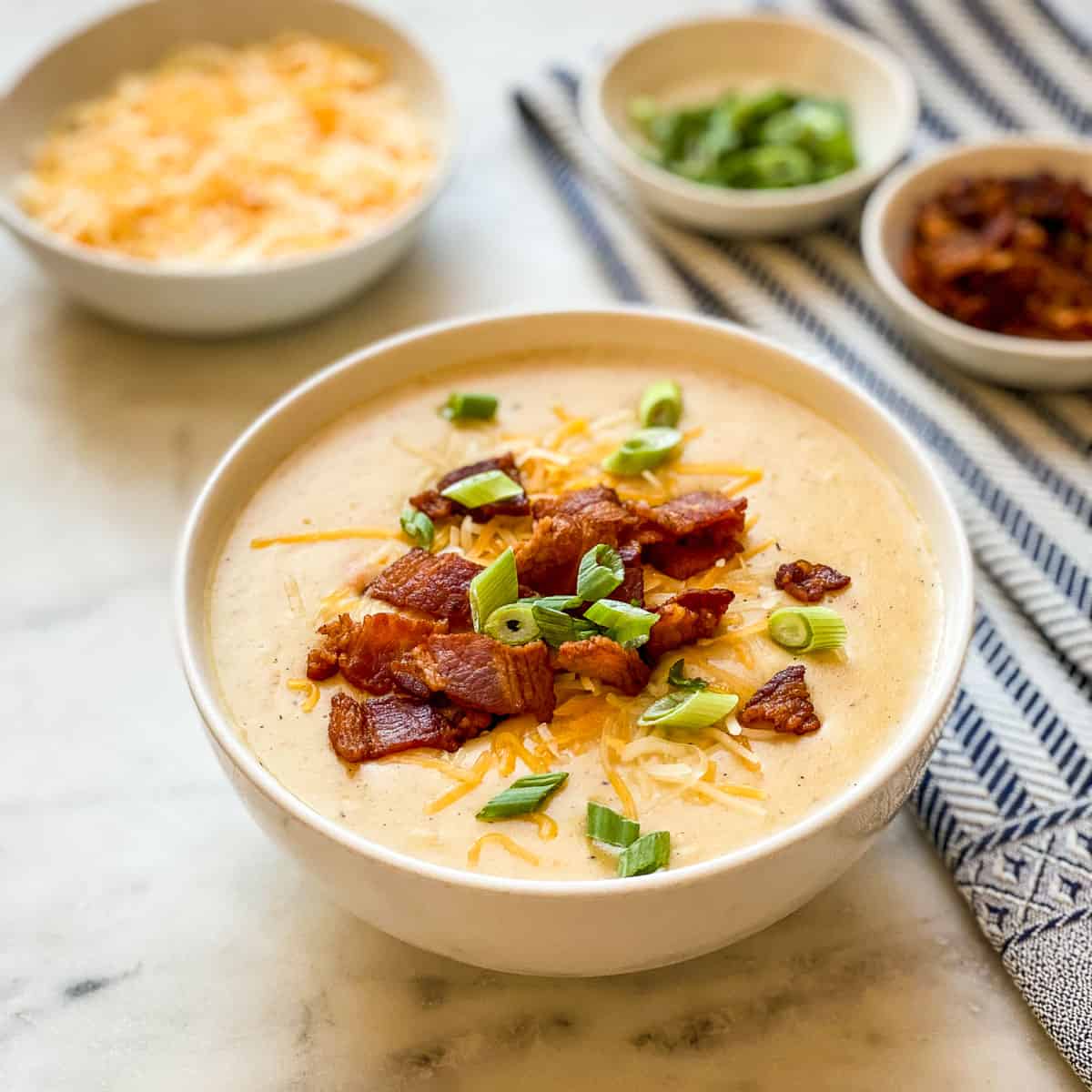 A bowl of Cheesy Potato Soup with Bacon show with various toppings.