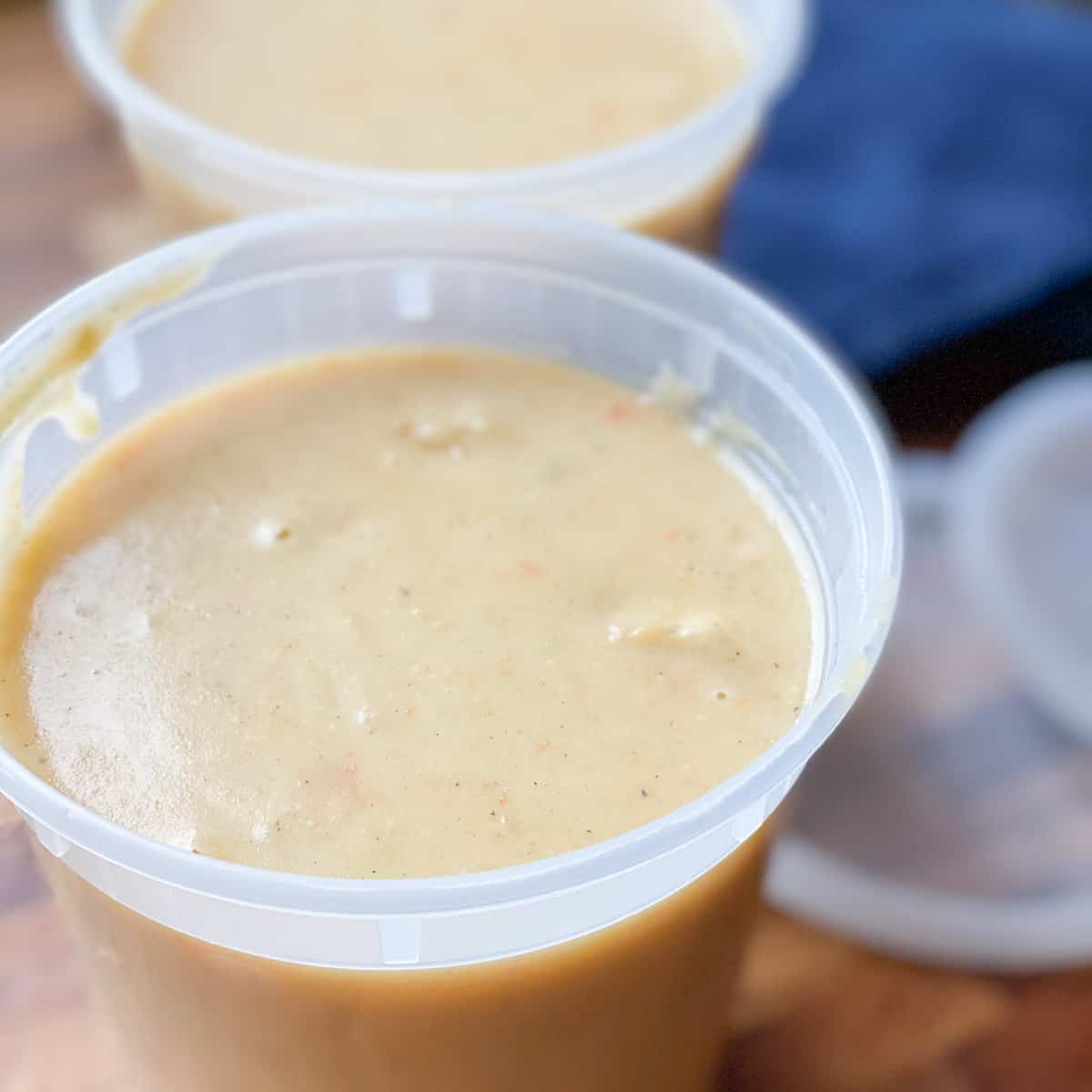 Image of potato soup in storage containers with lids and blue towel on right hand side.
