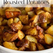 Crispy Oven Roasted Potatoes piled in a white bowl on a striped kitchen towel.