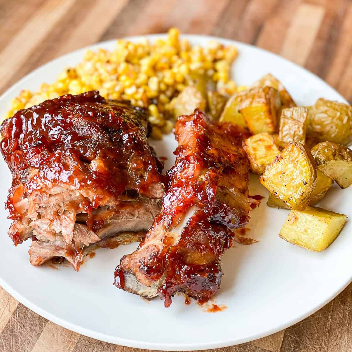 Oven Baked Ribs served on a white plate with Fried Corn and Roasted Potatoes.