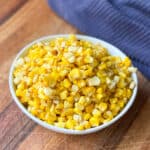 Fried Corn in a white bowl on cutting board with blue kitchen towel in upper right hand corner.