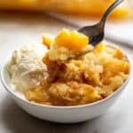Peach Dump Cake served in a white bowl with vanilla ice cream.