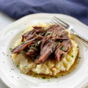 Juicy Pot Roast served on top of mashed potatoes pictured on a white plate with a fork.