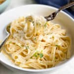 Fettuccine Alfredo in a white bowl with fork lifted for bite.