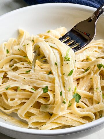 Fettuccine Alfredo in a white bowl with fork lifted for bite.
