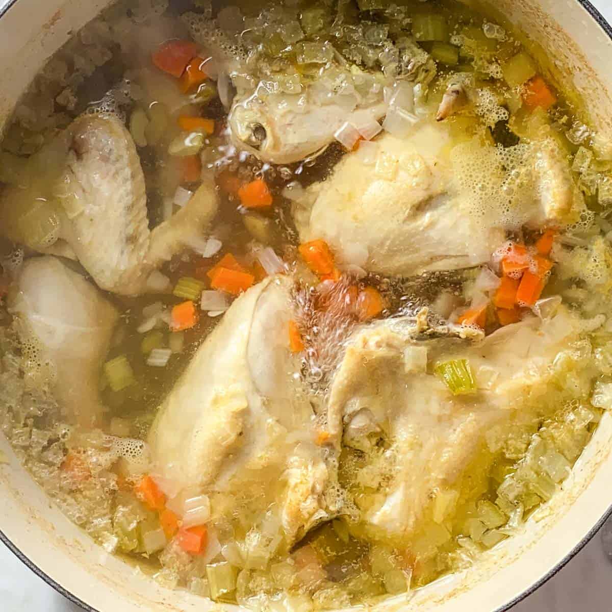Image of Homemade Chicken Soup simmering in a large cream colored Le Creuset Dutch Oven.