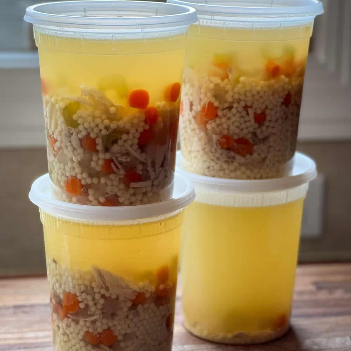 Image showing four quarts of Instant Pot Chicken Soup stacked two by two in restaurant storage containers.