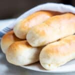 Image showing five buttery garlic breadsticks wrapped in a white and blue striped kitchen towel.