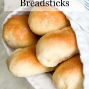 Pinterest pin showing five buttery garlic breadsticks wrapped in a white and blue striped kitchen towel.with banner title.