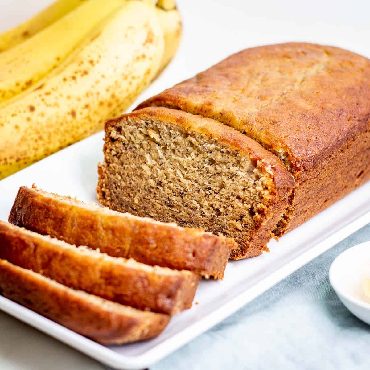 Sliced loaf of freshly baked banana bread with bananas on side.
