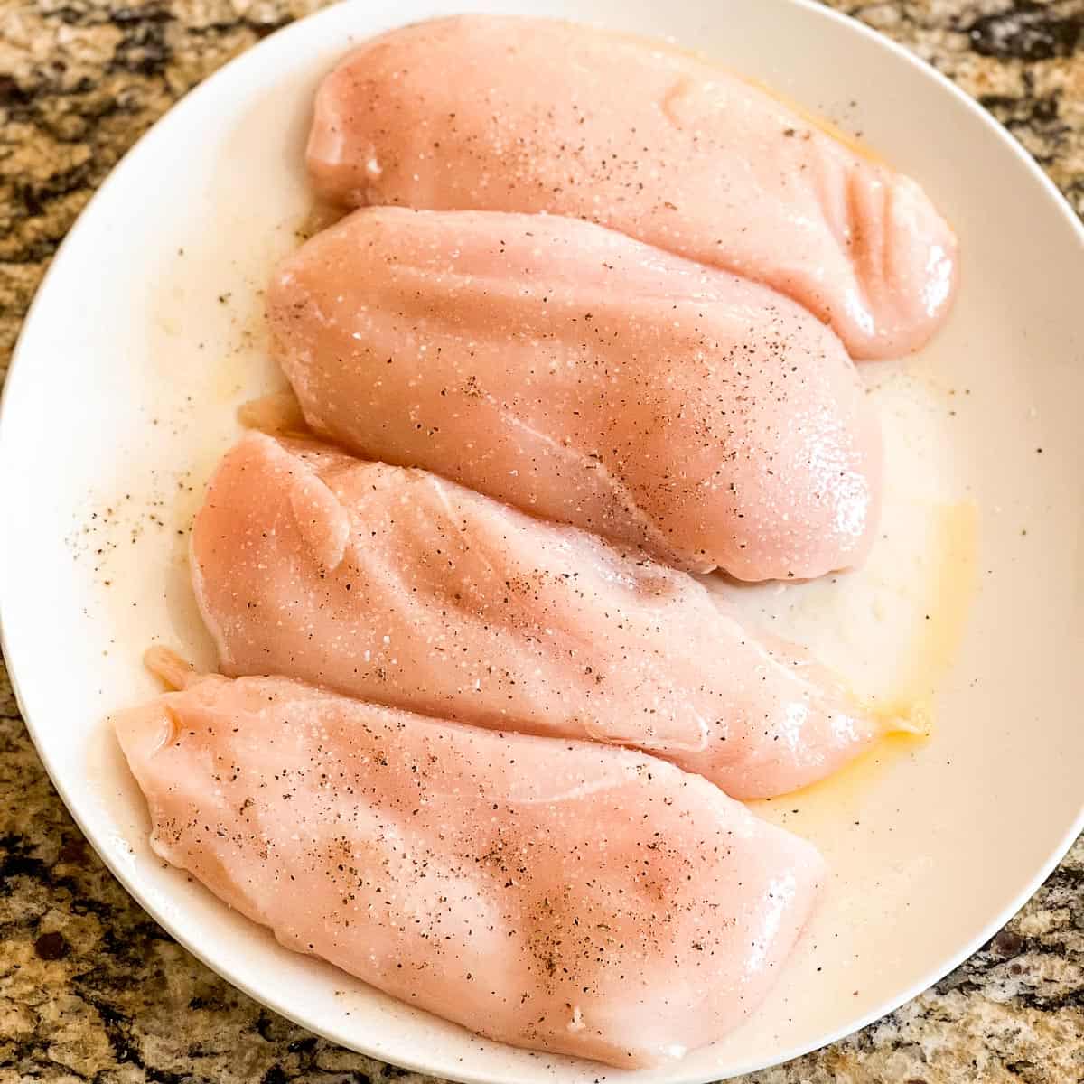 4 seasoned boneless, skinless chicken breast filets on a white plate.
