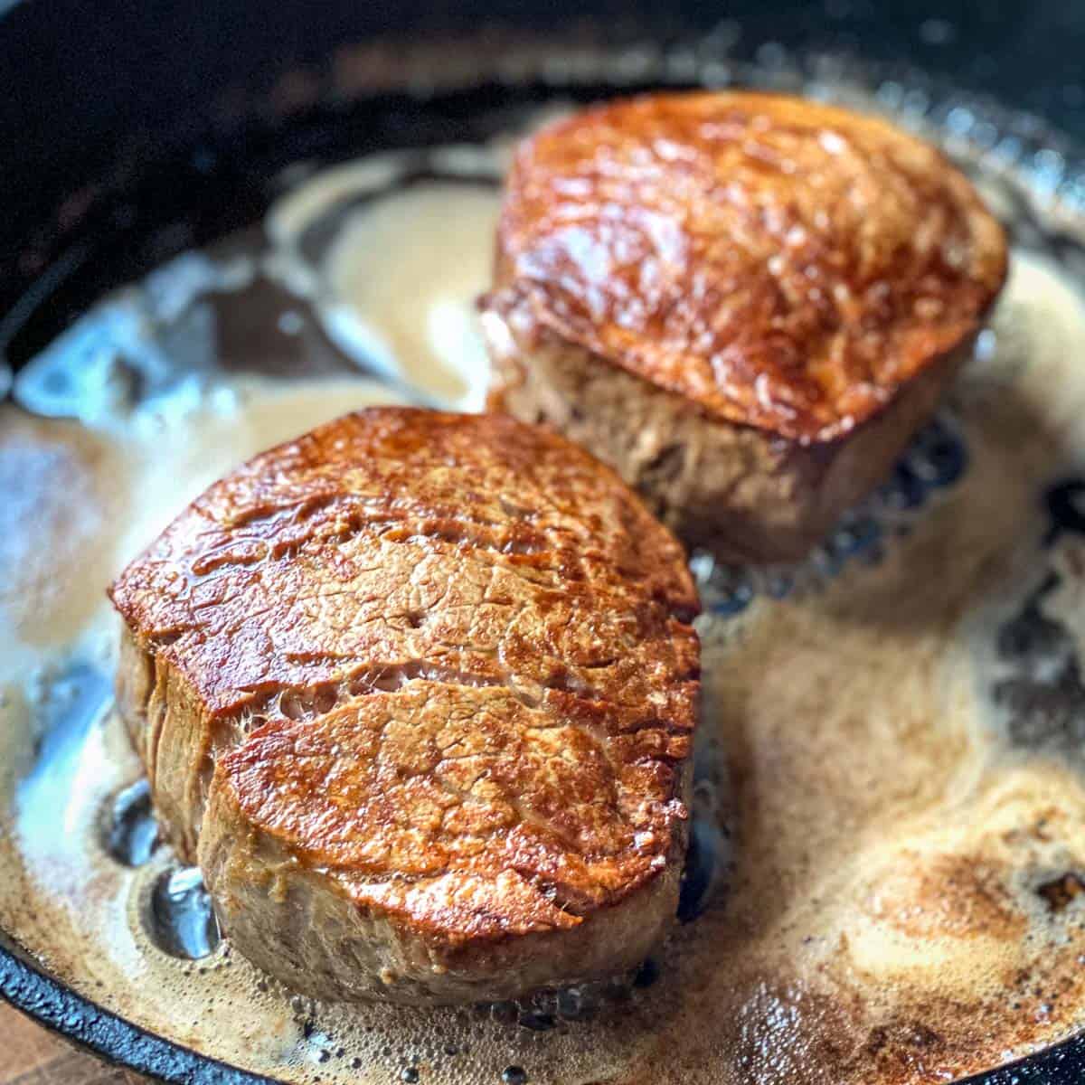 Two pan seared Filet Mignon steaks in cast iron skillet with brown butter.