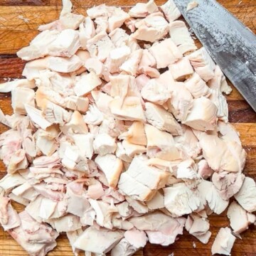 Cut up rotisserie chicken on a cutting board with knife.