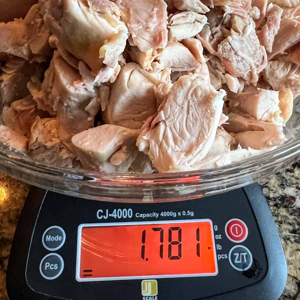 Cut up rotisserie chicken in a clear bowl on a digital scale.