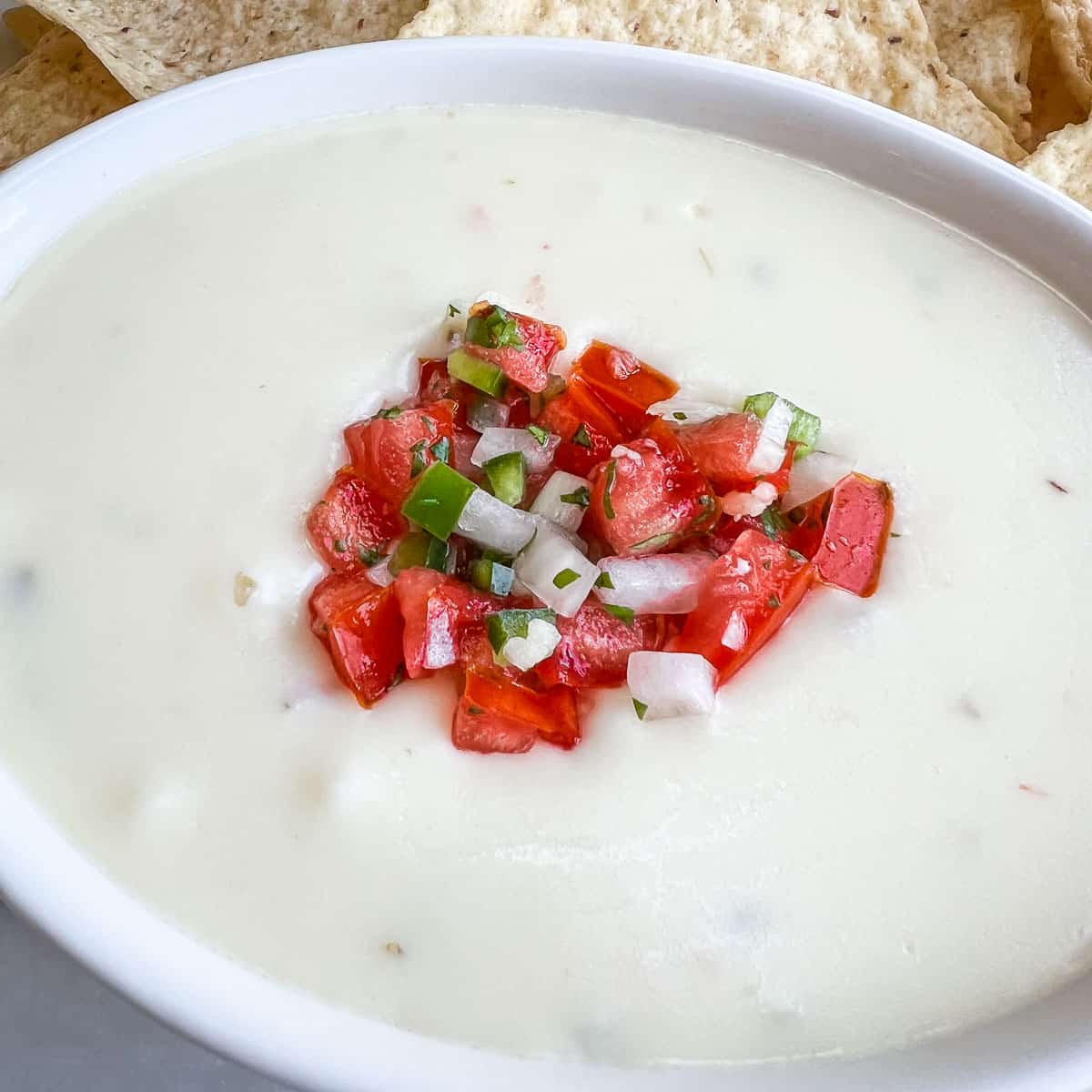 White Queso Dip topped with Pico de Gallo served in a white bowl with chips on the side.