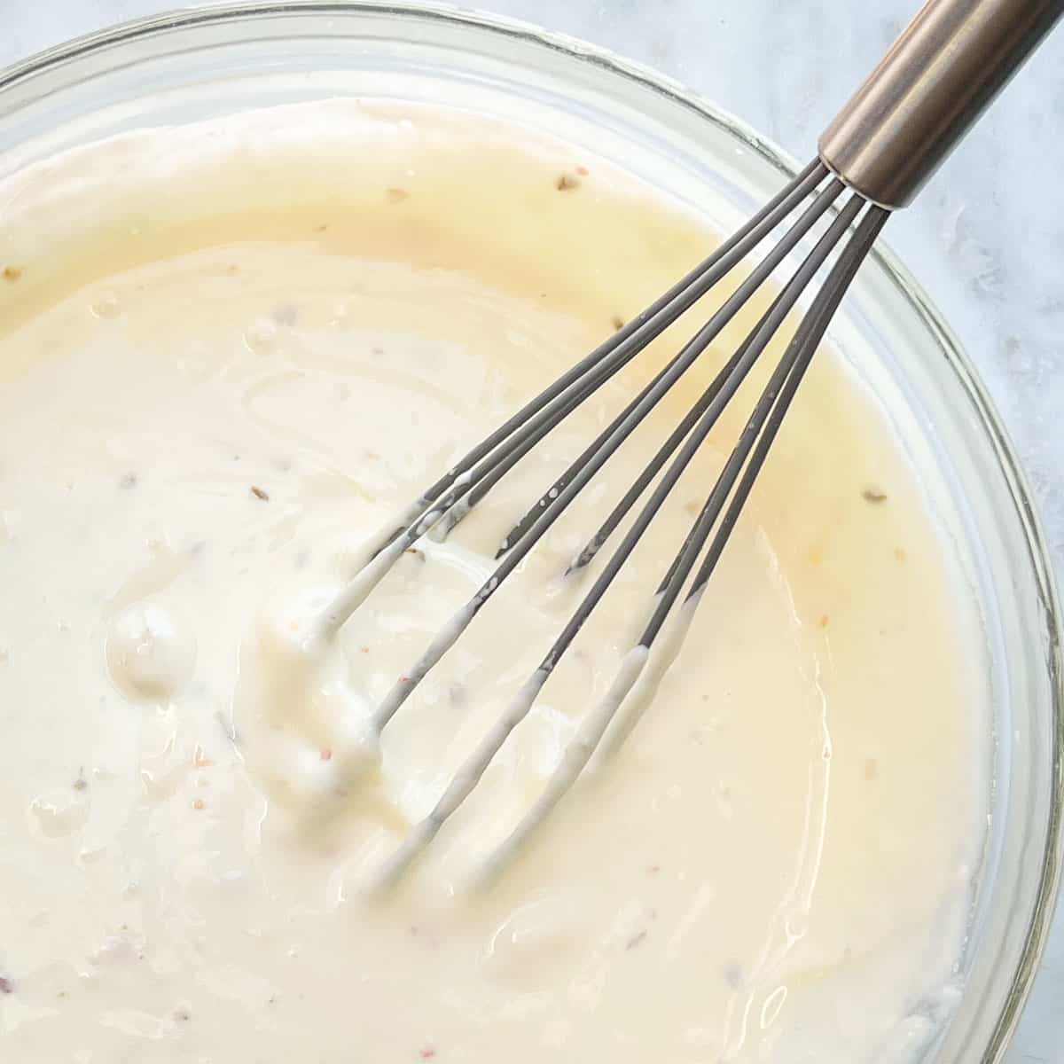 White Queso Dip in clear mixing bowl with whisk.