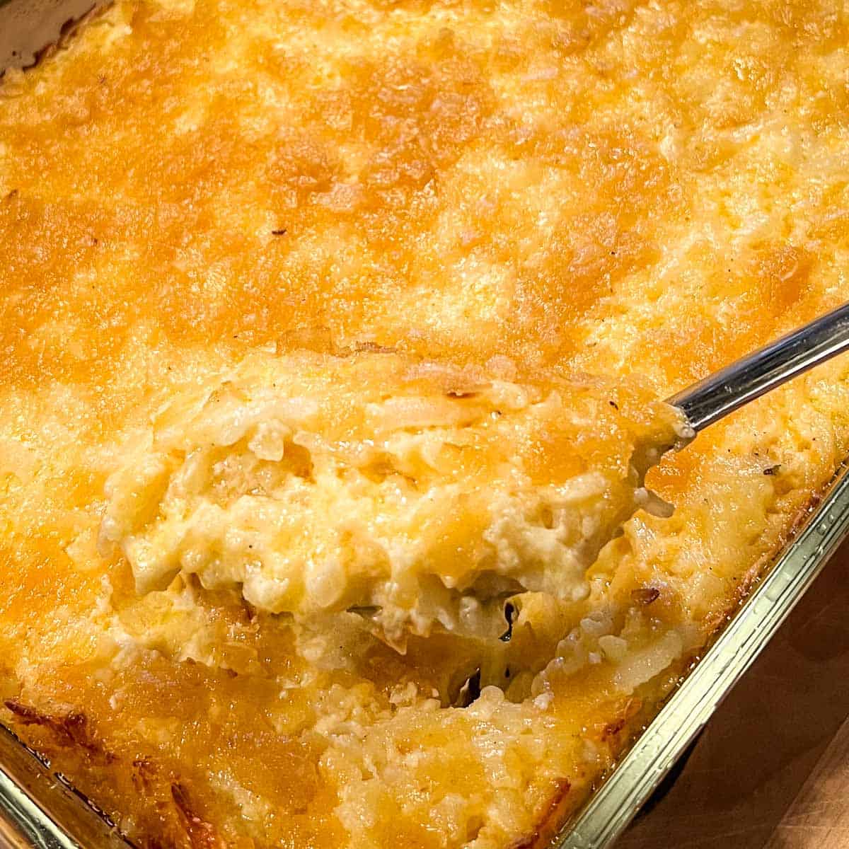Spoon raised from a pan of Cheesy Hashbrown Casserole.