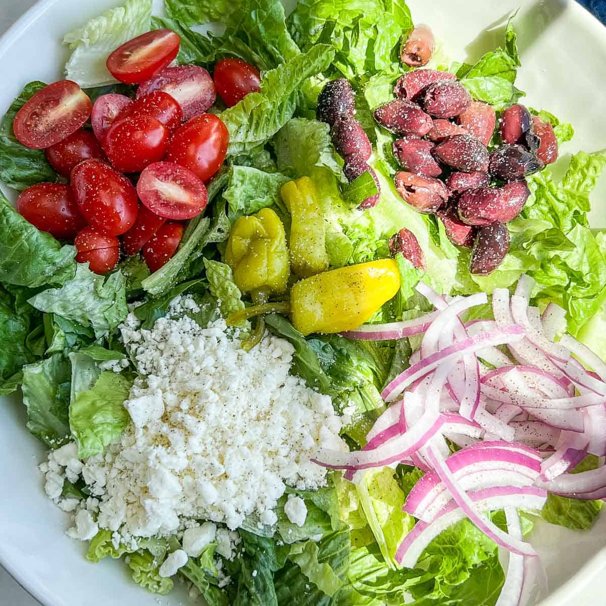 Copycat Panera Greek Salad individual ingredients arranged on a bed of romaine lettuce.