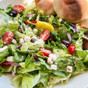 Copycat Panera Greek Salad in a big white bowl with fresh pita bread on the side.