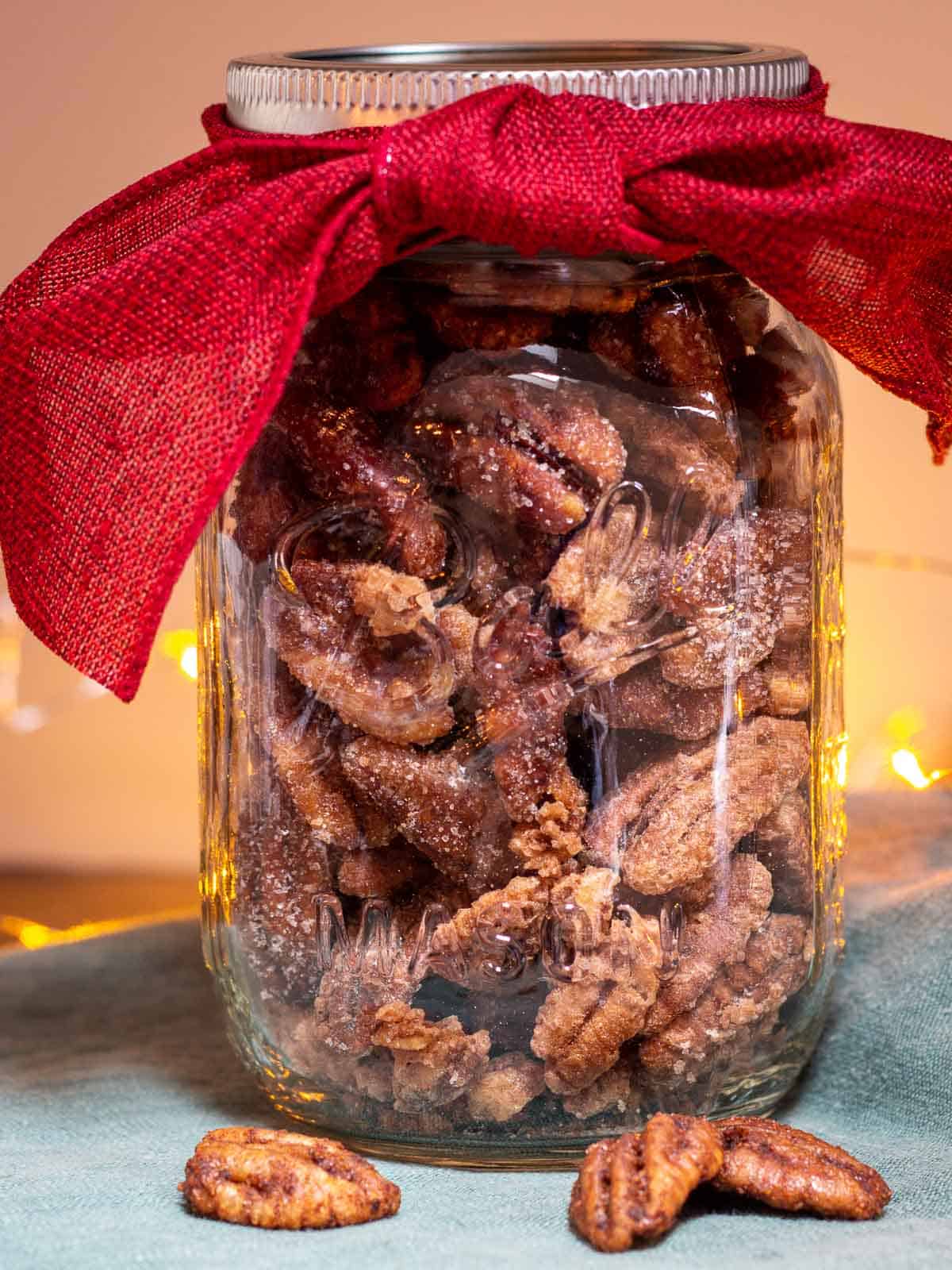 Air Fryer Candied Pecans in a mason jar with a red bow sitting on a green napkin with twinkle lights in background.