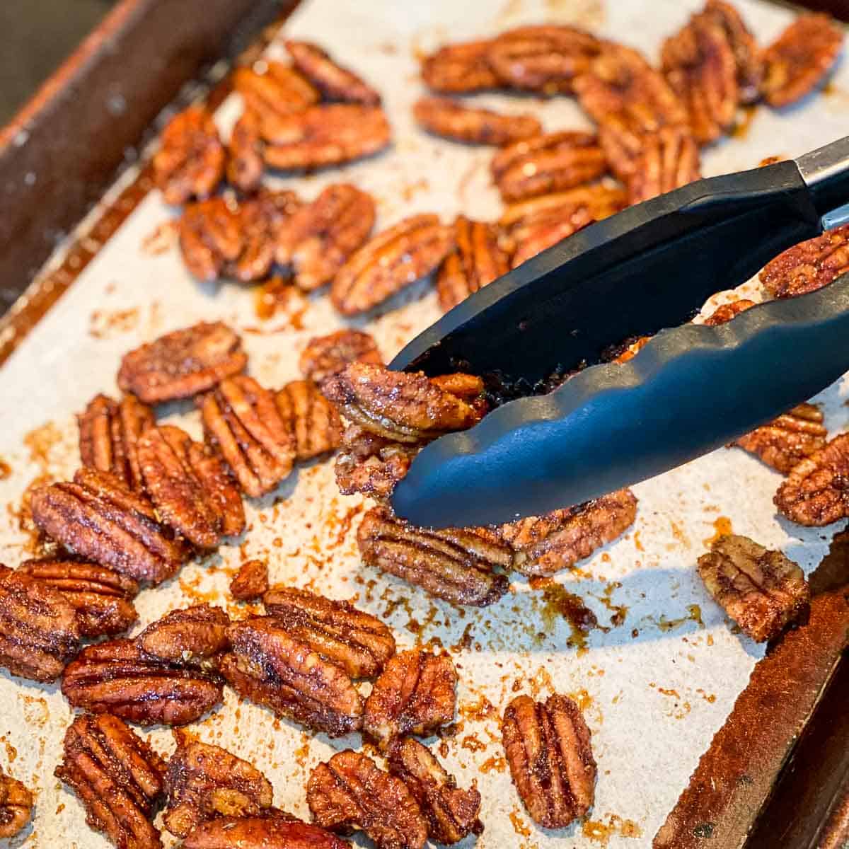 Air fryer candied pecans being placed on a cookie sheet lined with parchment paper.