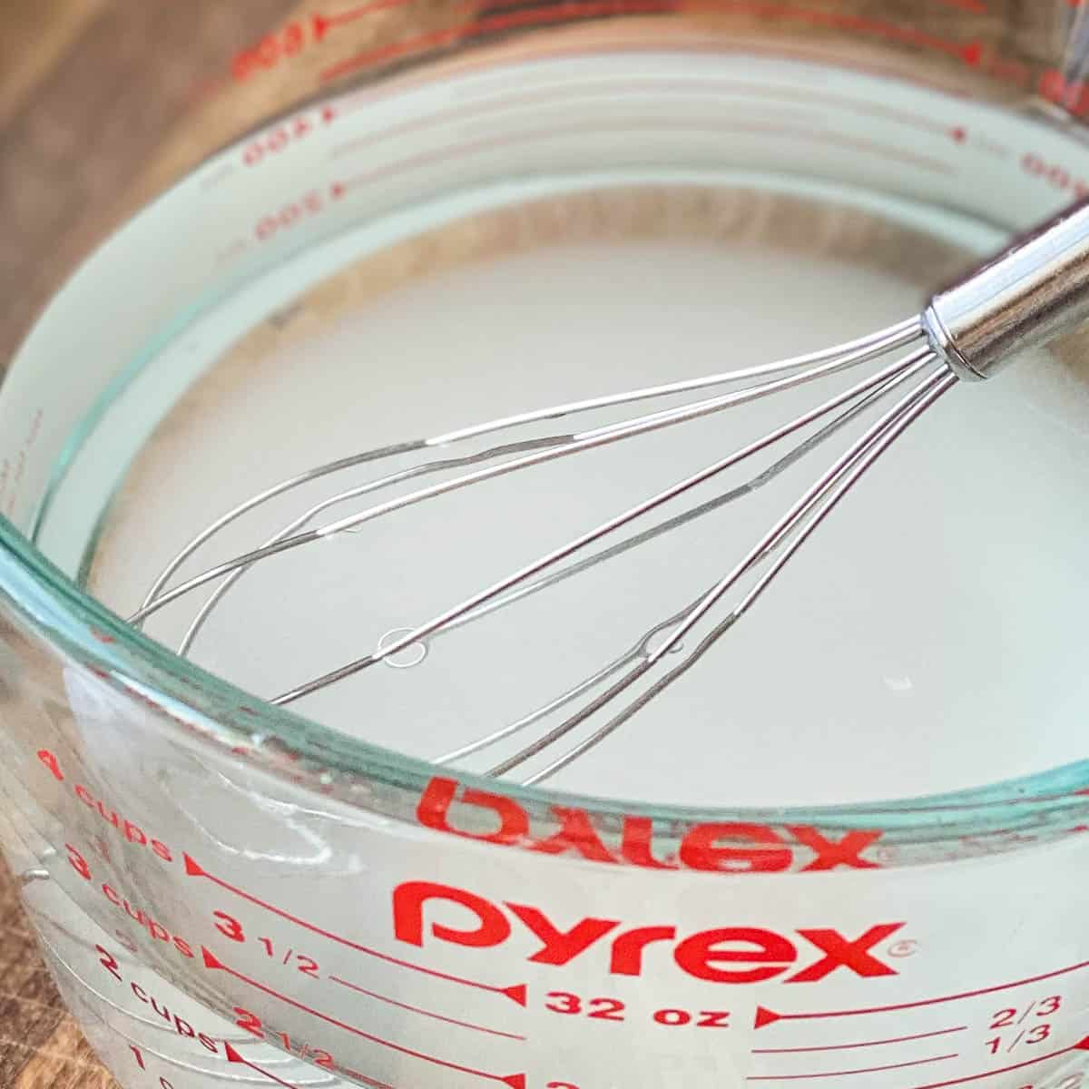 Simple syrup in a liquid measuring cup with a small whisk.
