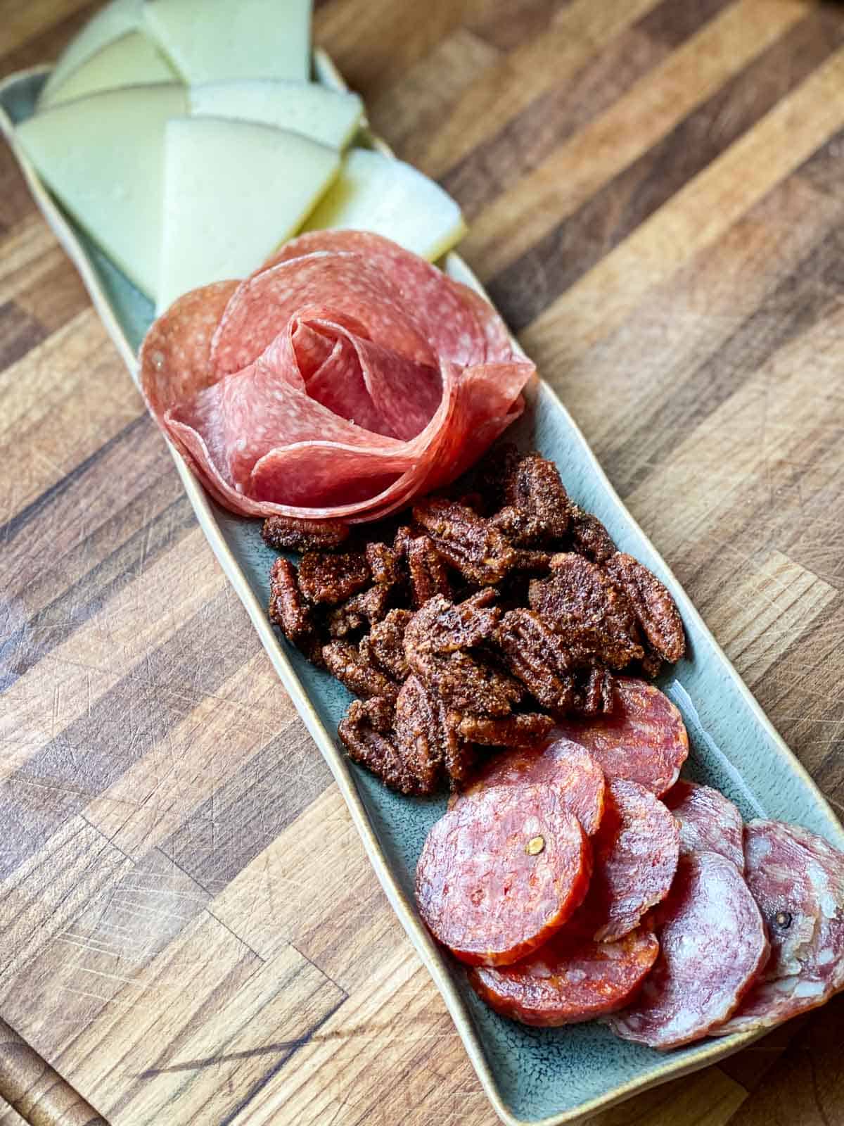 Small charcuterie board with meats and cheeses and candied pecans.