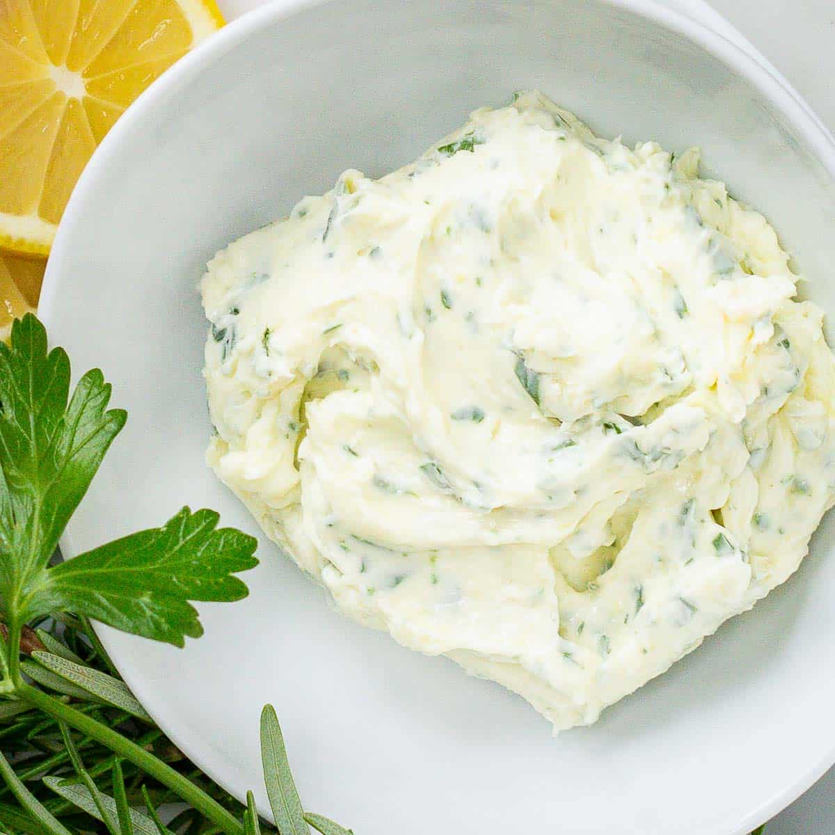 Herb butter in white dish with lemon and parsley on left side.