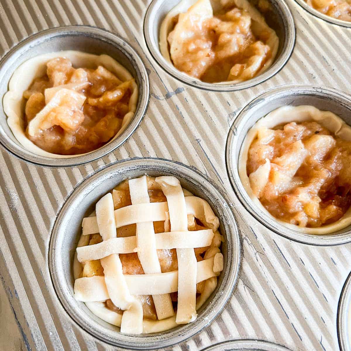 Lattice top on unbaked mini apple pie in a muffin tin.