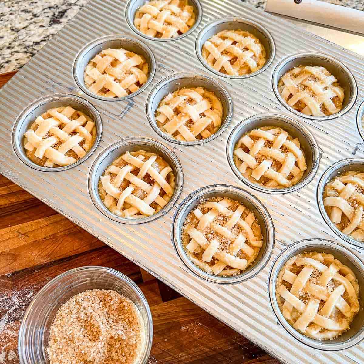 A muffin tin full of unbaked mini apple pies with lattice top ready for the oven.