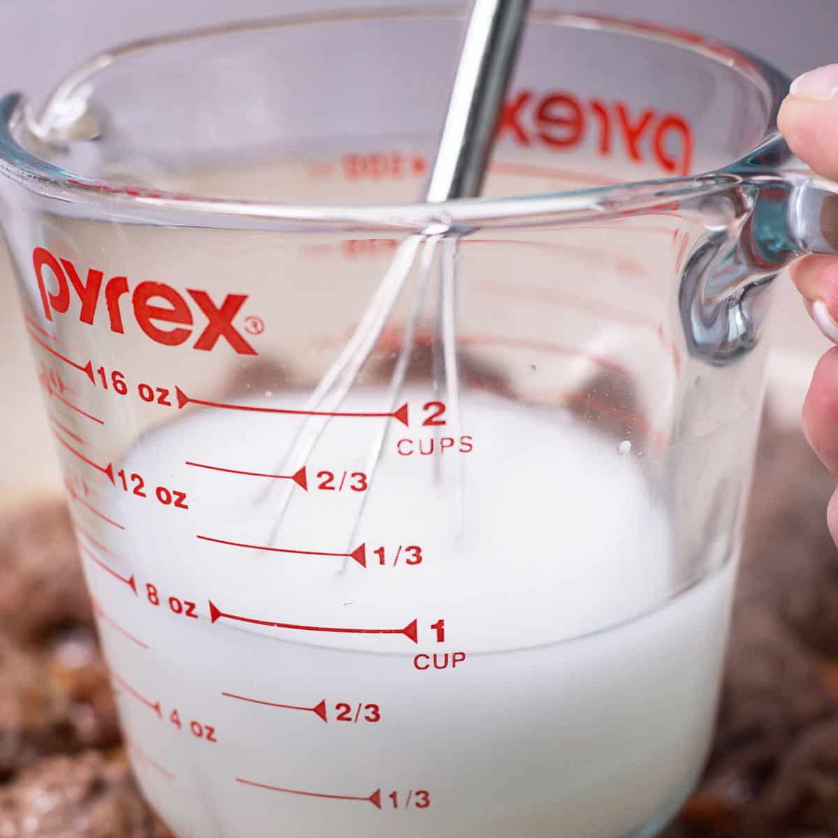 A slurry of water and corn starch in a glass pyrex measuring cup with a small whisk.