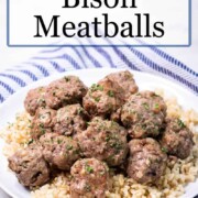Bison Meatballs over brown rice on a white plate with blue stripped kitchen towel in background.