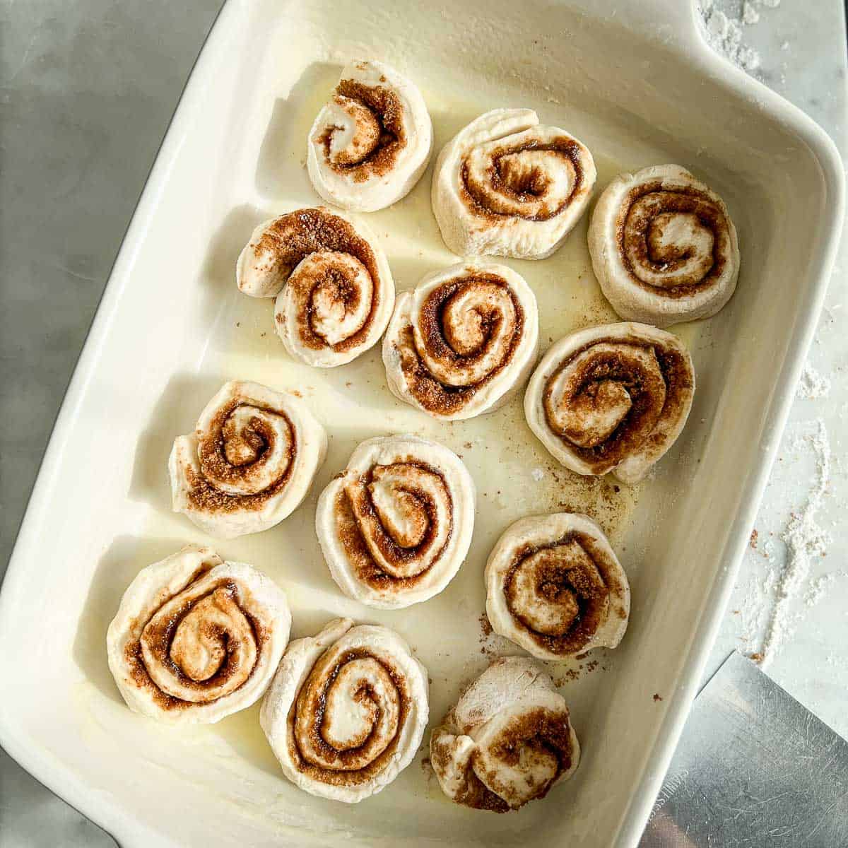 Unbaked cinnamon rolls transferred into a buttered baking dish.