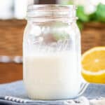 A mason jar half full of buttermilk with lemon wedge off to right side.