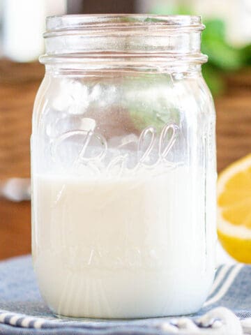 A mason jar half full of buttermilk with lemon wedge off to right side.