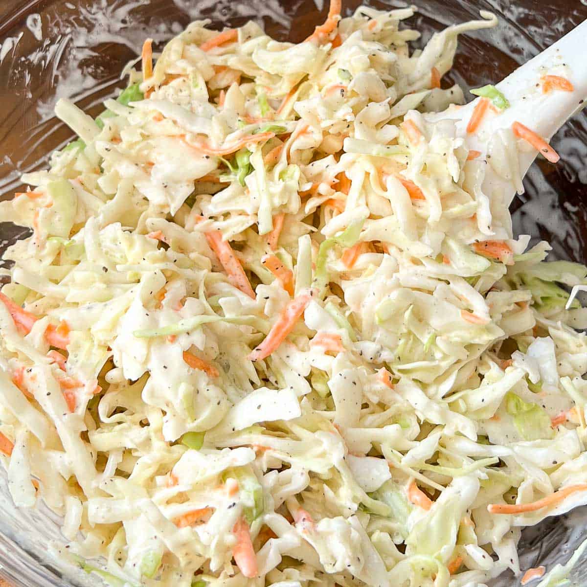 Coleslaw mixed together in a glass bowl with a white rubber spatula in bowl..
