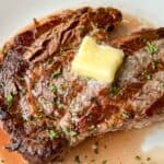 Juicy Grilled Ribeye with a pat of melting butter on top and garnished with herbs.
