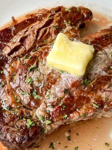 Juicy Grilled Ribeye with a pat of melting butter on top and garnished with herbs.