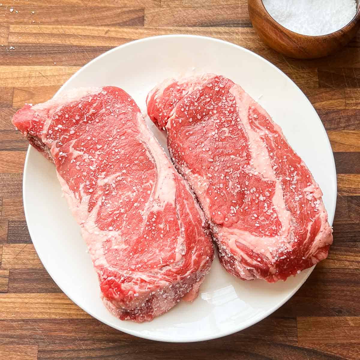 Salted Ribeye Steak on a white plate.