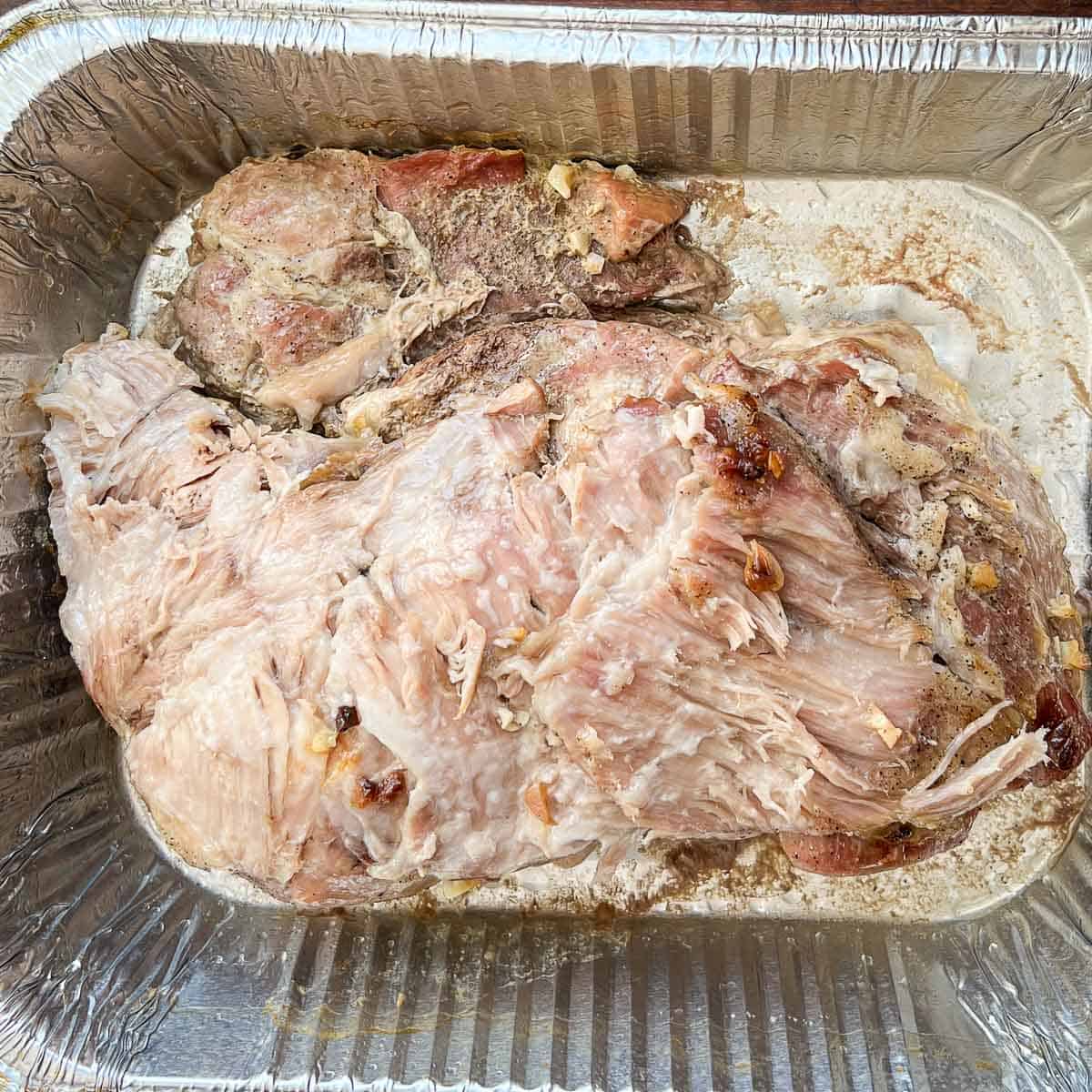Slow cooked pork with the fat cap removed resting inside a disposable roasting pan.