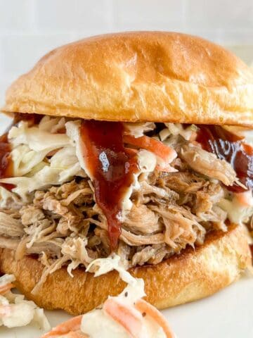 Pulled pork on a brioche bun with coleslaw and BBQ sauce dripping down the side.