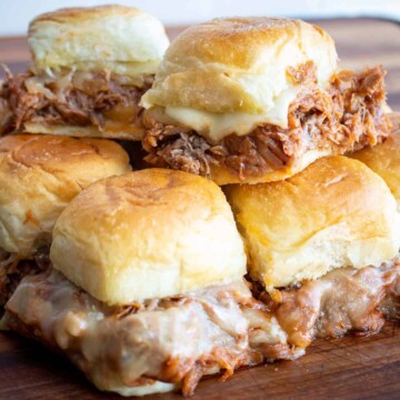 BBQ Pulled Pork Sliders stacked on a cutting board with melted cheese pull.